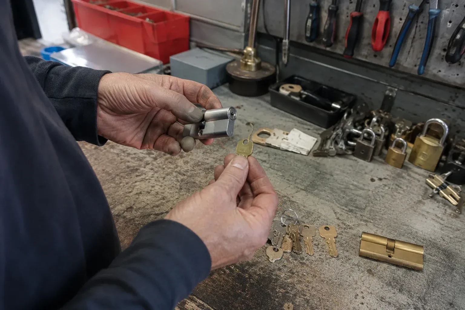 Hands holding a silver-colored lock cylinder and a brass-colored key above a workbench with padlocks, keys and tools. — Master Key System Design, Barrie